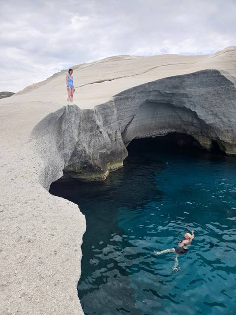 A coastal area with rocky formations and a person swimming in clear blue water.