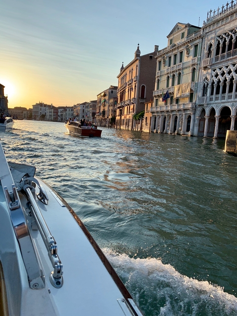 Boats on a canal with buildings in the background at sunset.
