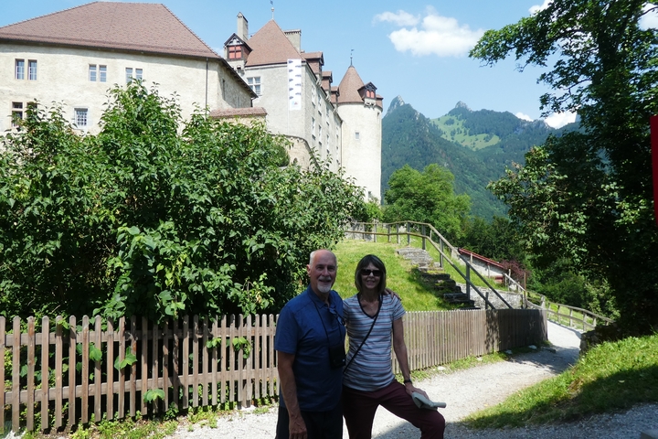 A couple posing in front of a castle with mountains in the background.