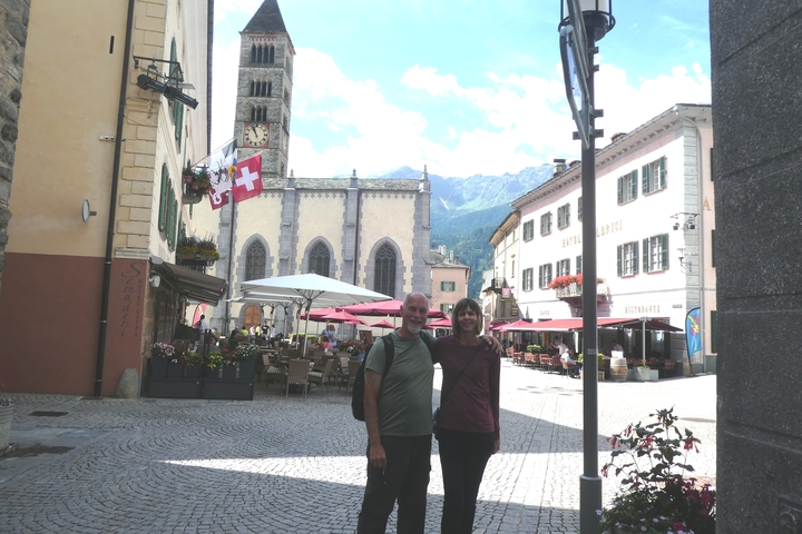 Couple standing in a quaint town square with a church and flags.