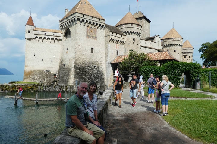 A couple posing in front of a large historic castle with a moat.