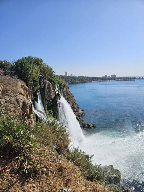       Waterfall cascading into the sea with the city skyline.
  