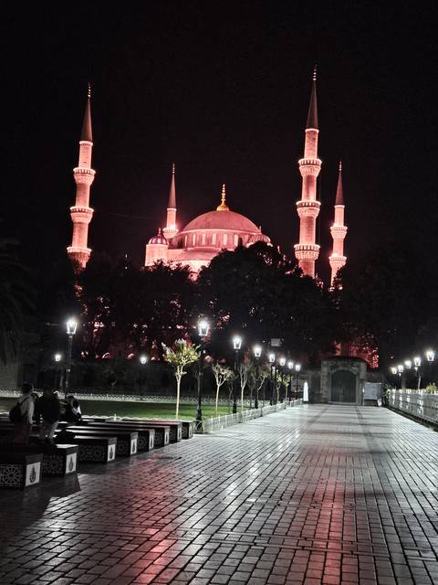       Illuminated mosque with multiple minarets at night.
  