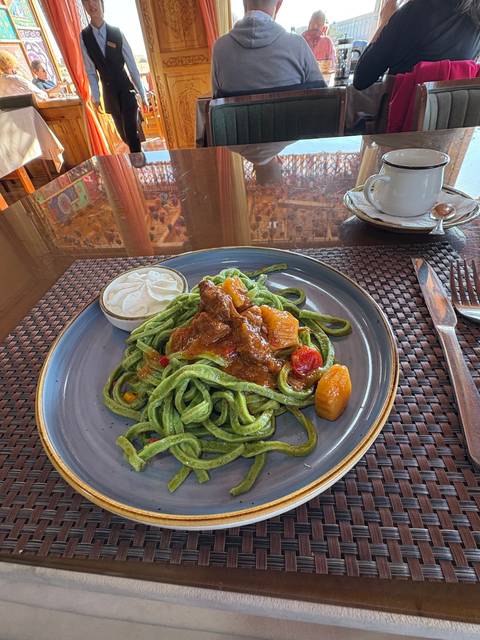 Plate of green pasta with sauce, served at a restaurant.