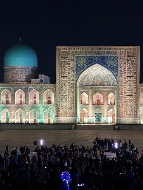 Night view of a lit, decorated building with a crowd.