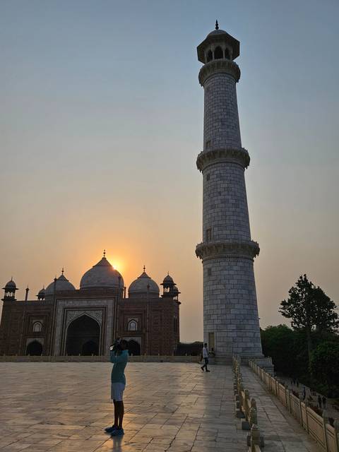       A person taking a photo of the Taj Mahal minaret at sunset.
  