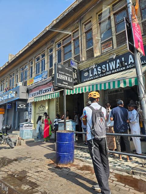       People walking past shops with signs in an urban setting.
  