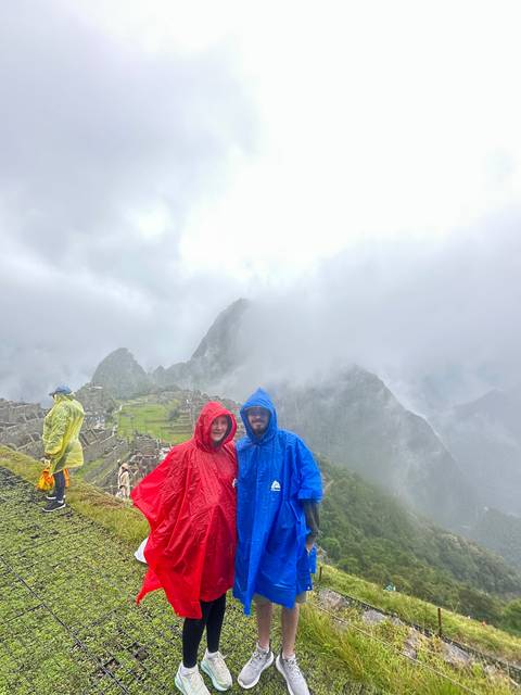 Two people wearing rain ponchos with a foggy Machu Picchu behind.