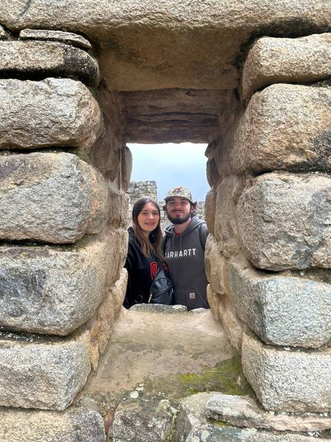 A couple smiling through an ancient stone window at Machu Picchu.