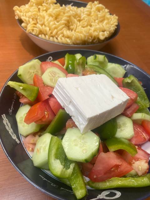 Plate with Greek salad and another with pasta.