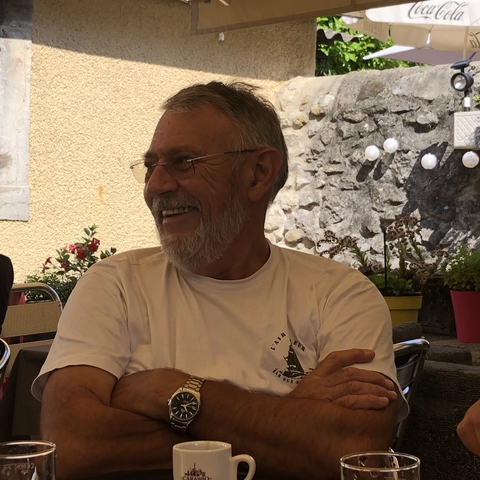 Smiling elderly man sitting at a table in an outdoor café.