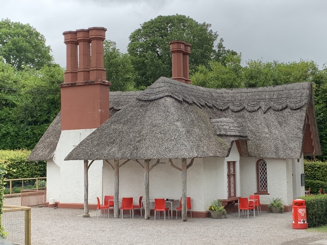       Charming thatched-roof cottage with red accents surrounded by greenery.
  