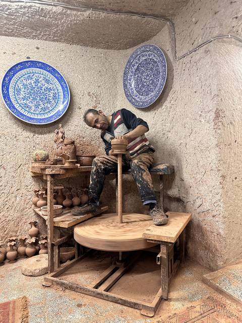       Man working on pottery wheel with ceramic plates around.
  