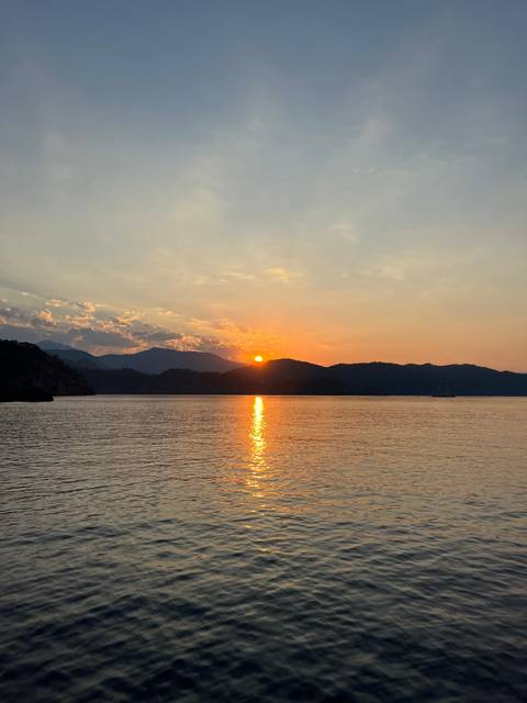       Serene sunset over the sea with a view of distant mountains.
  