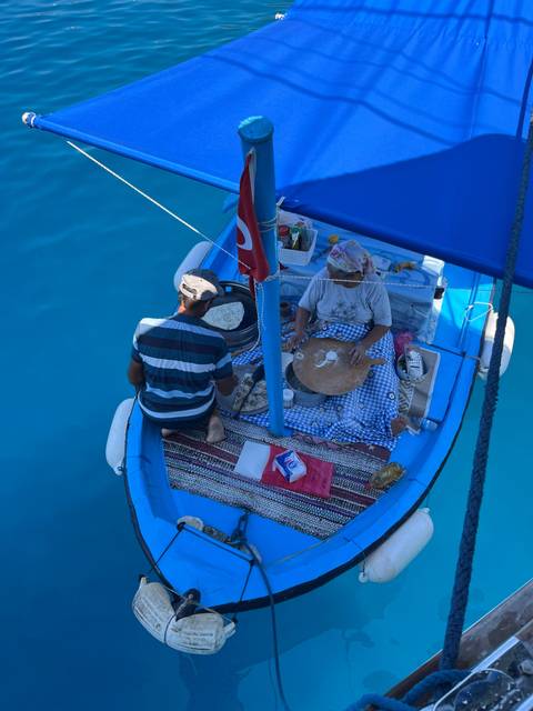       Two people preparing traditional food on a boat.
  