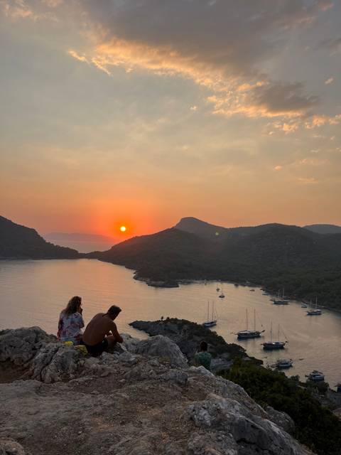       Sunset view over a bay with yachts and mountains.
  