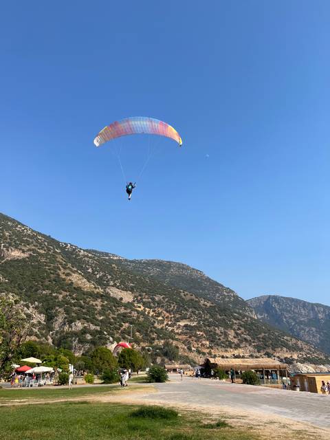       Person paragliding against a clear blue sky over mountainous terrain.
  