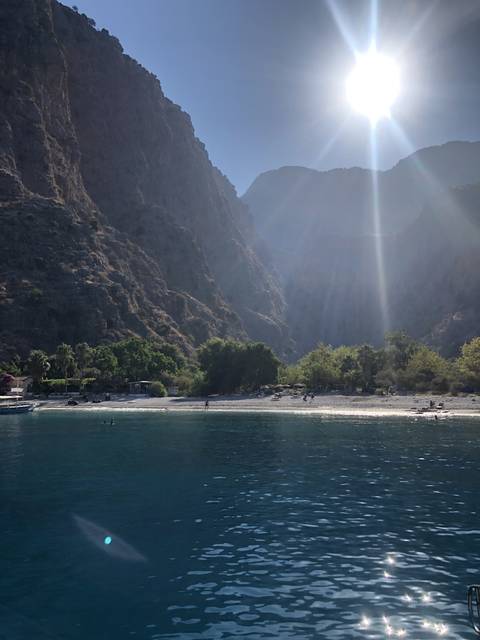       A sunny beach with clear waters and mountain backdrop.
  