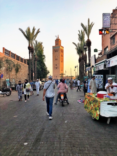 Street scene in Morocco with people and a tall tower.