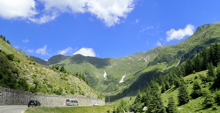 Lush mountainous landscape with a winding road and vehicles.
