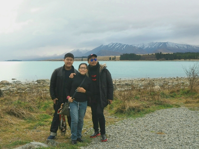 Family posing by a lake with snow-capped mountains in the background.