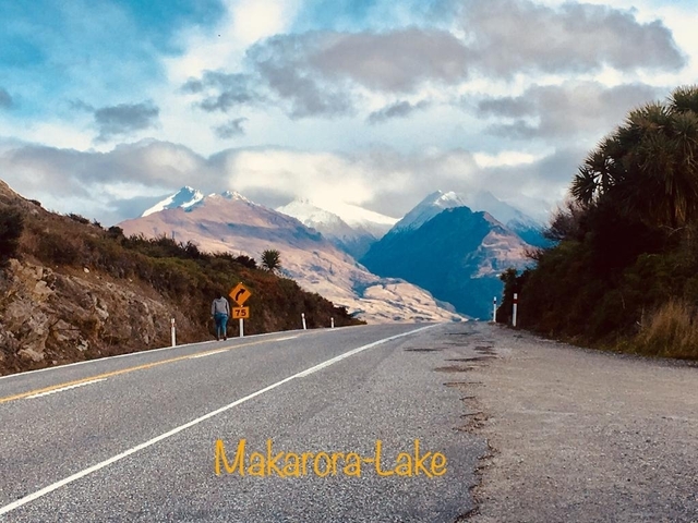 Road leading towards snow-covered mountains under cloudy skies.