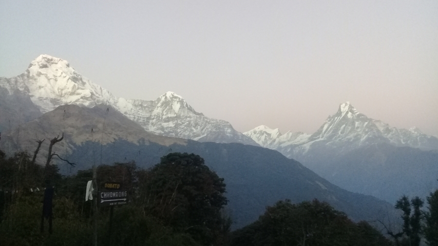 Himalayan mountain range under a clear sky with a signpost in the foreground.