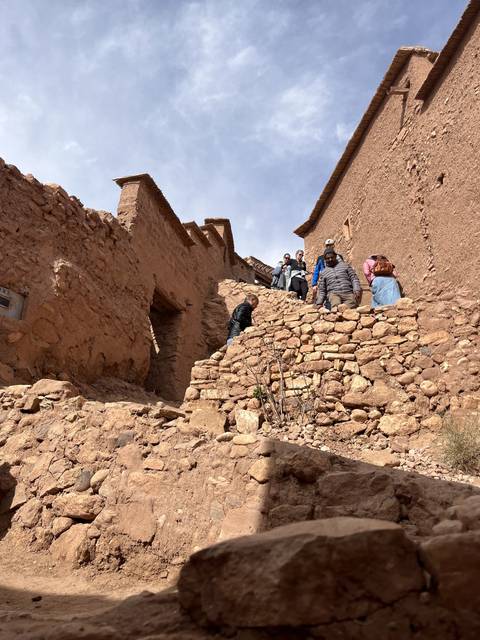       People sitting on steps of an ancient building.
  