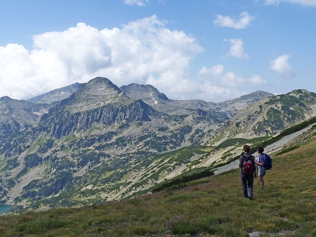      Hikers walking along mountain range with green vegetation.
  