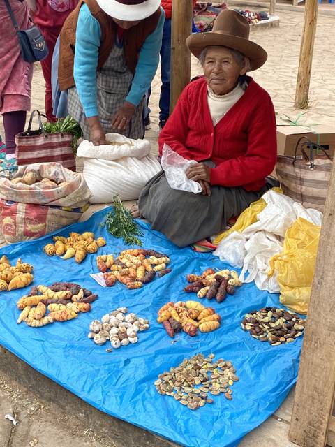 Two people sitting at a market stall with colorful produce displayed.
