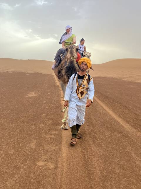       People riding camels across a vast desert landscape.
  