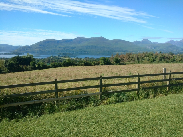 A rural landscape with fields, a fence, and distant mountains.