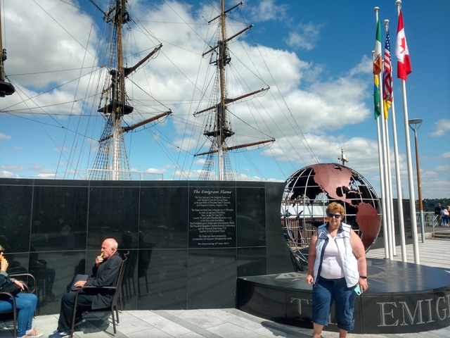       A woman and a man in front of a monument with a ship in the background.
  