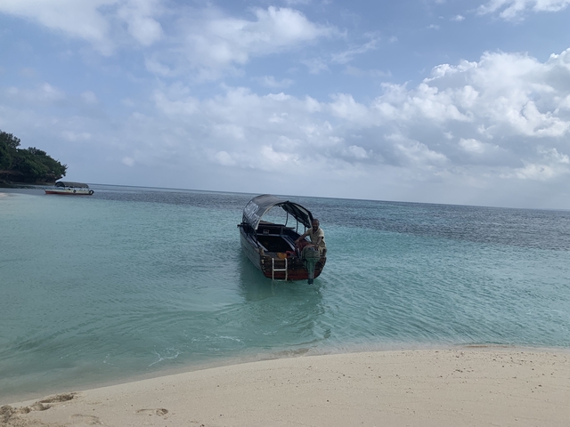 Boat on clear blue ocean water near a sandy beach.