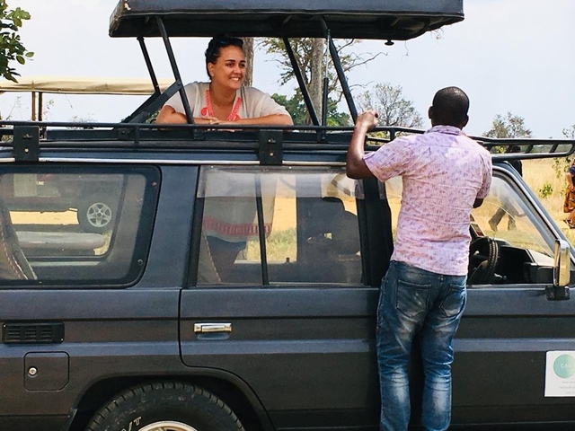 Two people interacting beside a safari vehicle.