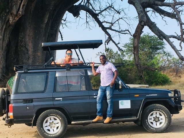 A man and a woman posing with a safari vehicle and a large baobab tree.