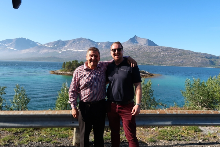 Two people posing by a scenic lake with mountains.