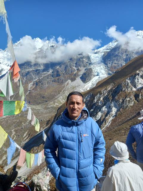 A person stands in front of snowy mountains and prayer flags.