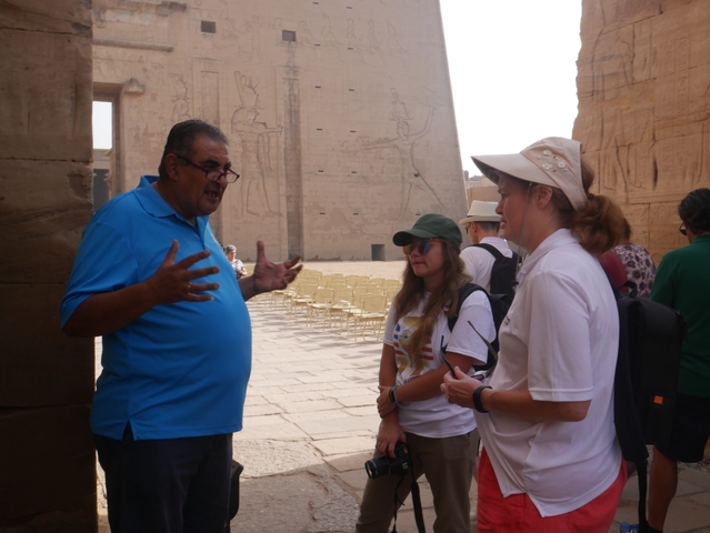       A group of people engaged in an outdoor discussion near ancient structures.
  