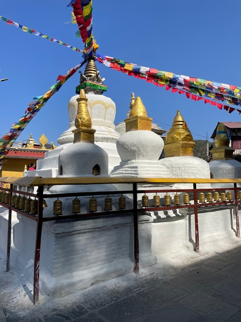 White and gold stupa surrounded by prayer wheels and flags.