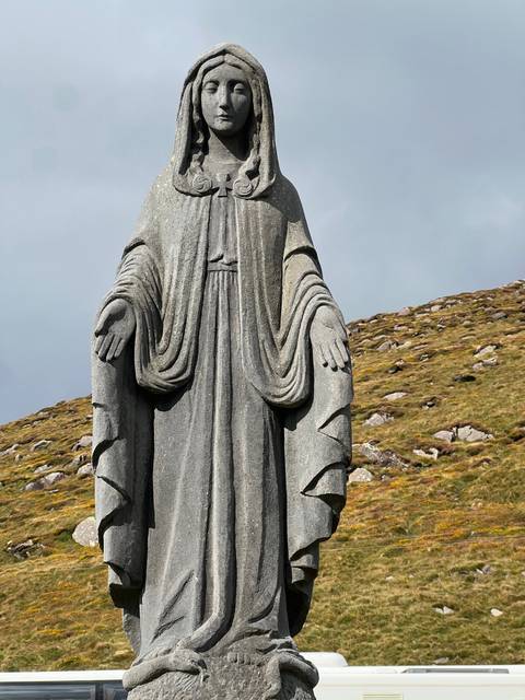 A stone statue of a robed figure against a grassy landscape.