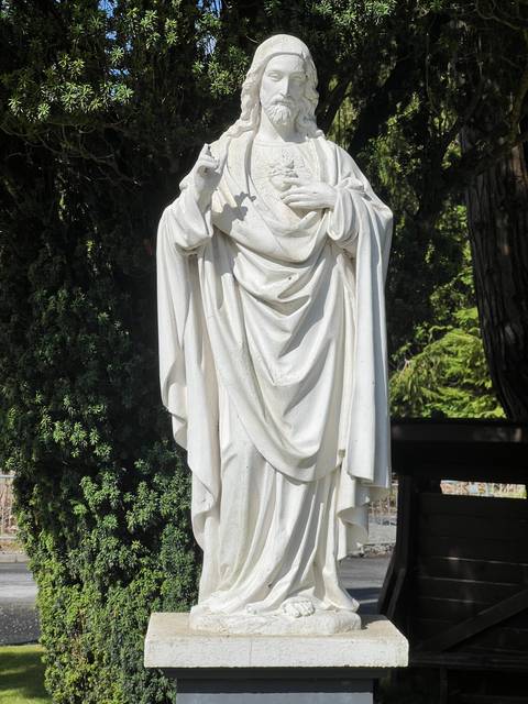       White stone statue of a religious figure surrounded by greenery.
  