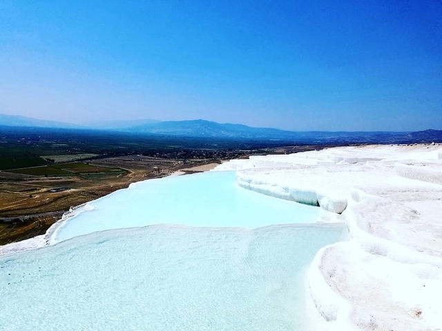 White terraces of Pamukkale with a pool of blue water.