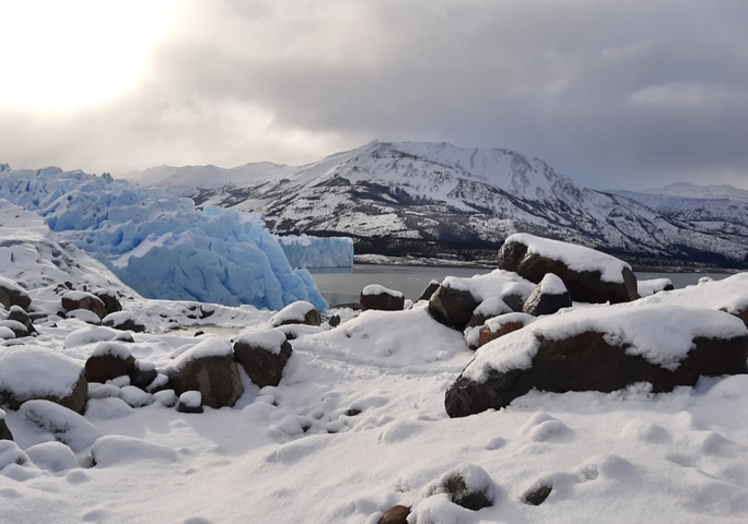 Impressive blue glacier with snow-covered rocks in the foreground.