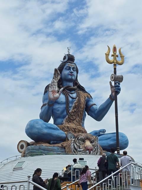       Large statue of a deity against the sky with people around.
  