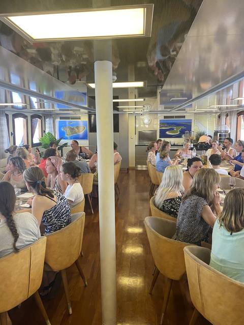 People seated indoors at dining tables on a ship.