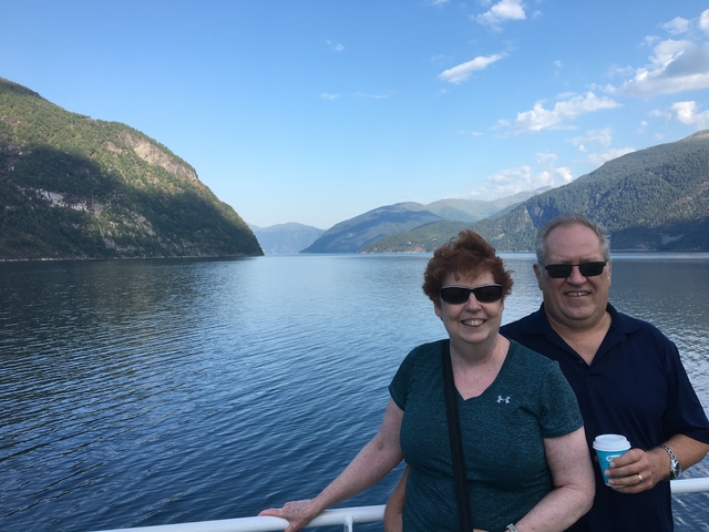 Couple posing on a ferry with mountains and water in the background.