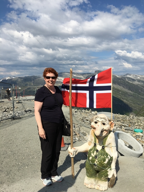 Woman standing next to a Norwegian flag in a mountainous area.