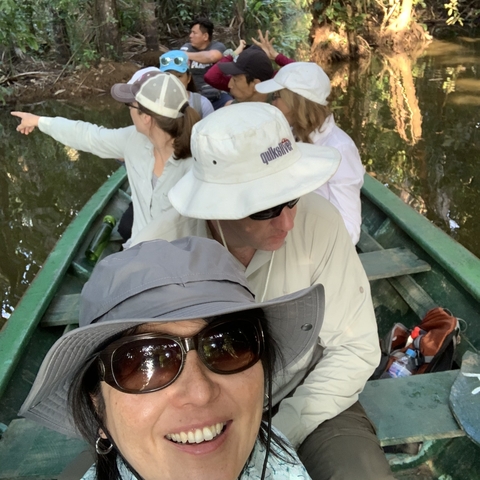 A group of people in a canoe navigating a jungle waterway, wearing sunglasses and hats.