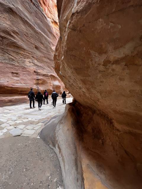      Narrow path through canyon with people walking.
  